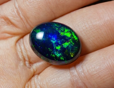 Opale noire luisante, éclatant du vert émeraude au bleu abyssal, avec une face arrière tout aussi étincelante, ornée d'une pointe noire