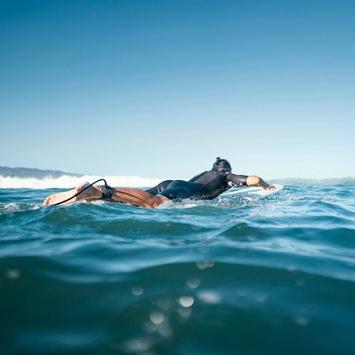 Comment faire du surf ? Le guide complet pour les débutants 6 surfeur en train de ramer dans l'eau allongé sur sa planche