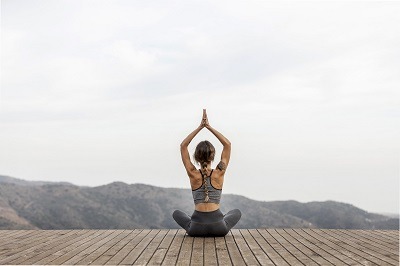 femme en position assise sur un ponton faisant du yoga en plain air