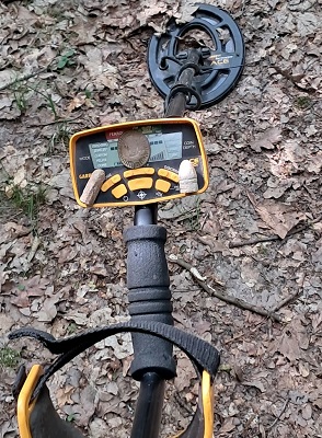 Personne utilisant un détecteur de métaux en lisière de forêt, cherchant des objets historiques.